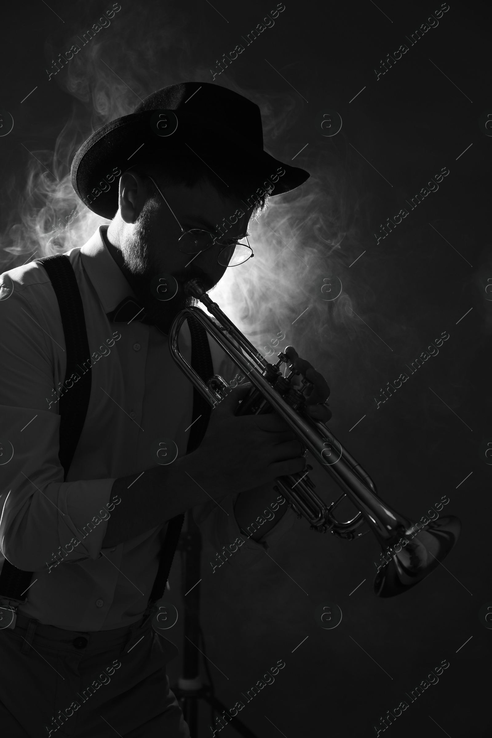 Photo of Professional musician playing trumpet on dark background with smoke. Black and white effect