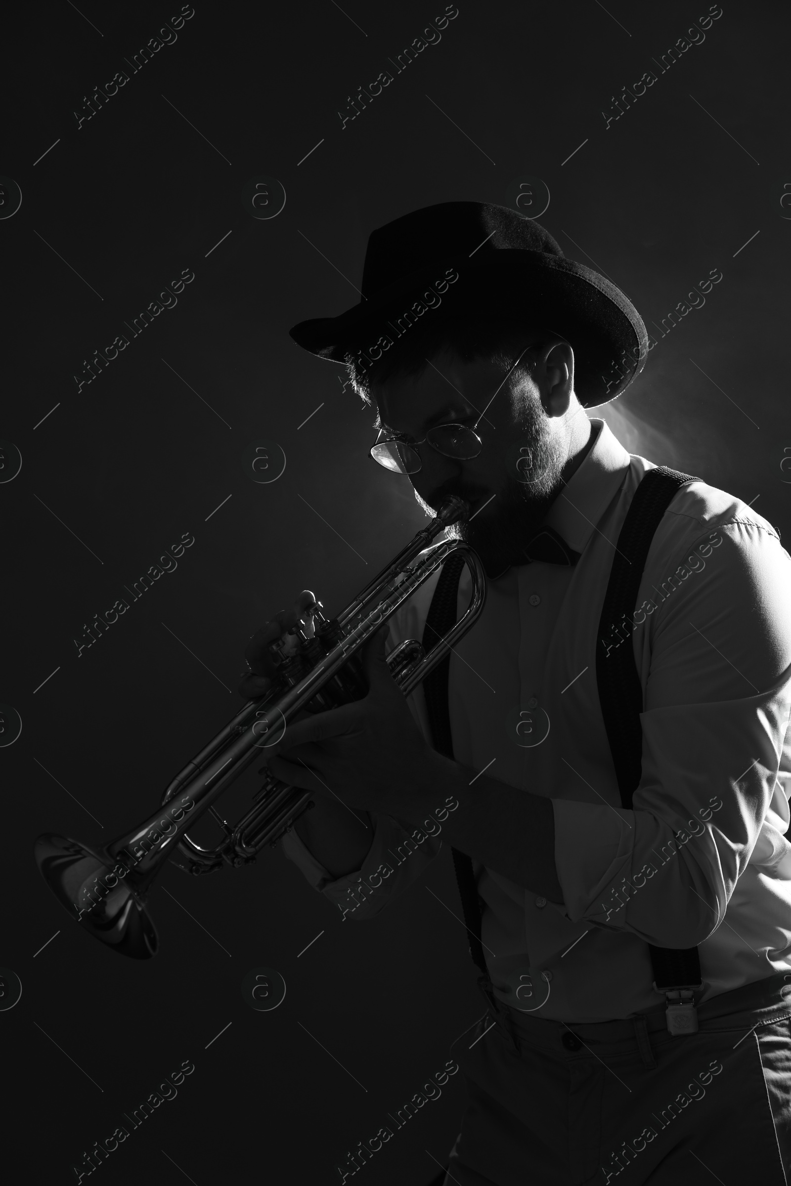 Photo of Professional musician playing trumpet on dark background. Black and white effect