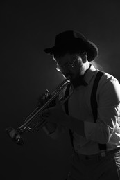 Photo of Professional musician playing trumpet on dark background. Black and white effect