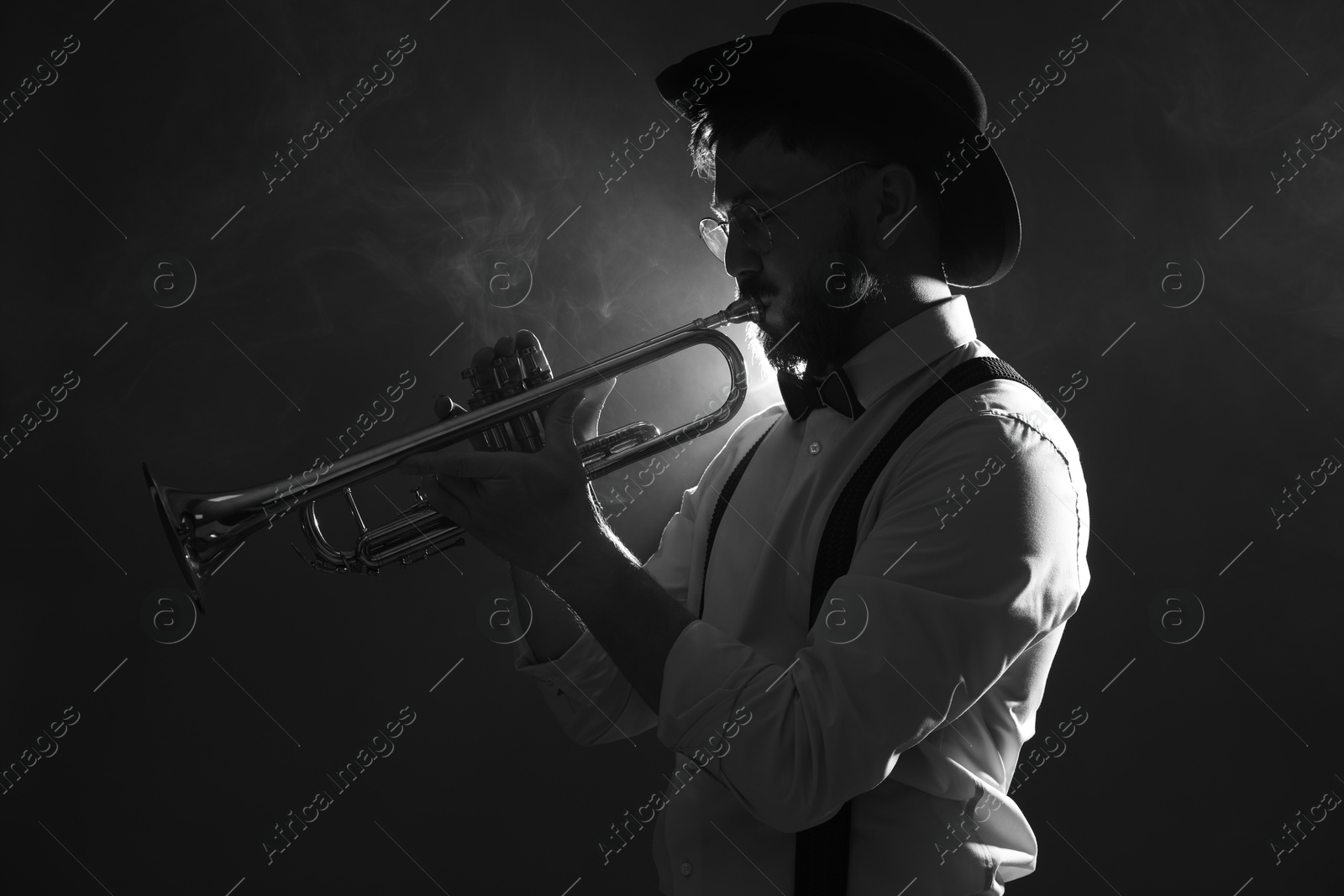 Photo of Professional musician playing trumpet on dark background with smoke. Black and white effect