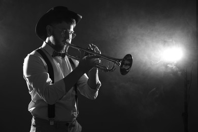 Photo of Professional musician playing trumpet on dark background with smoke, space for text. Black and white effect