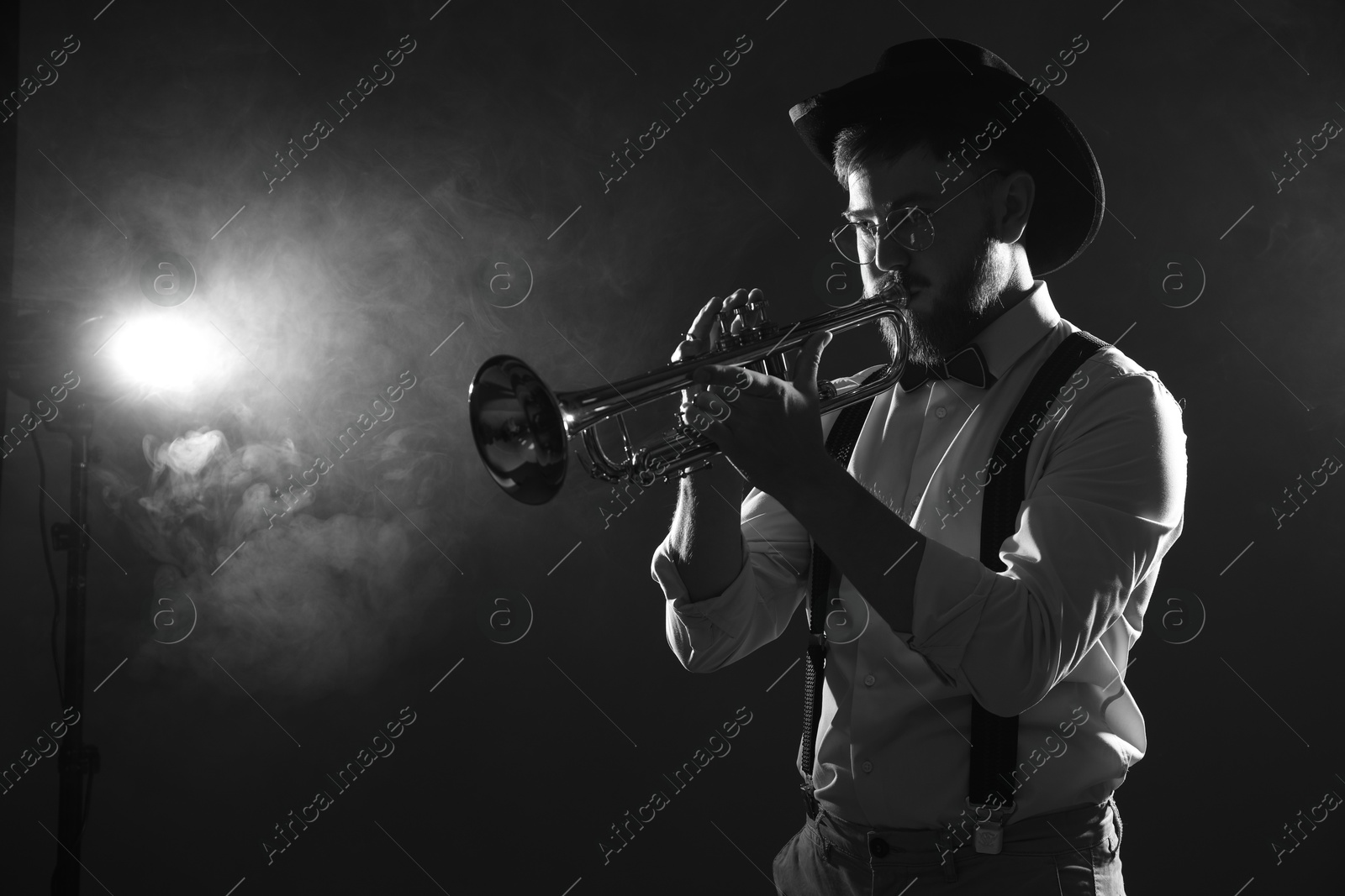 Photo of Professional musician playing trumpet on dark background with smoke, space for text. Black and white effect