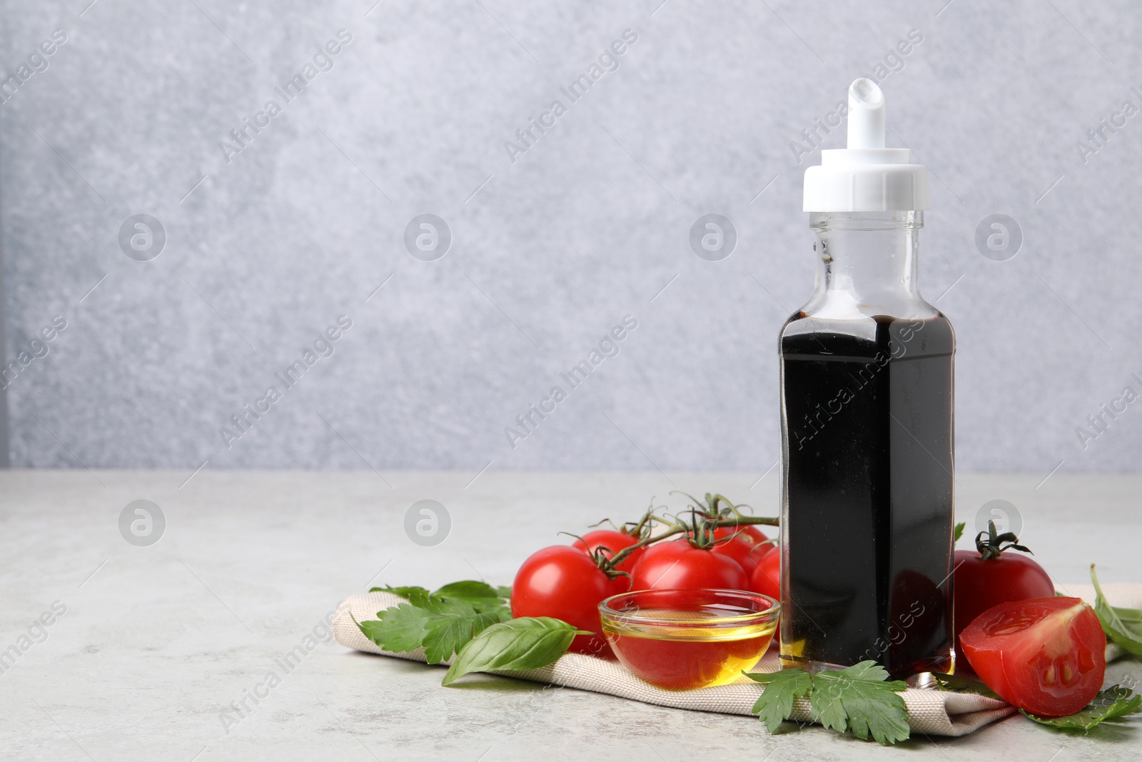 Photo of Bottle of balsamic vinegar, tomatoes, parsley and peppercorns on light grey table, space for text