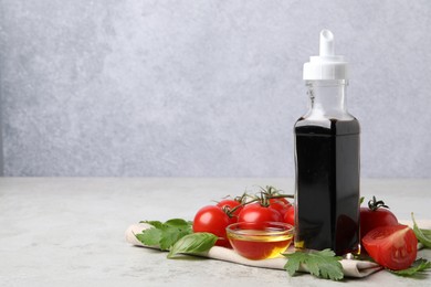 Photo of Bottle of balsamic vinegar, tomatoes, parsley and peppercorns on light grey table, space for text