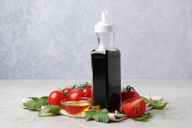 Bottle of balsamic vinegar, tomatoes, parsley and peppercorns on light grey table