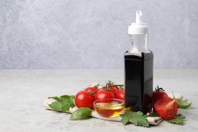 Photo of Bottle of balsamic vinegar, tomatoes, parsley and peppercorns on light grey table, space for text