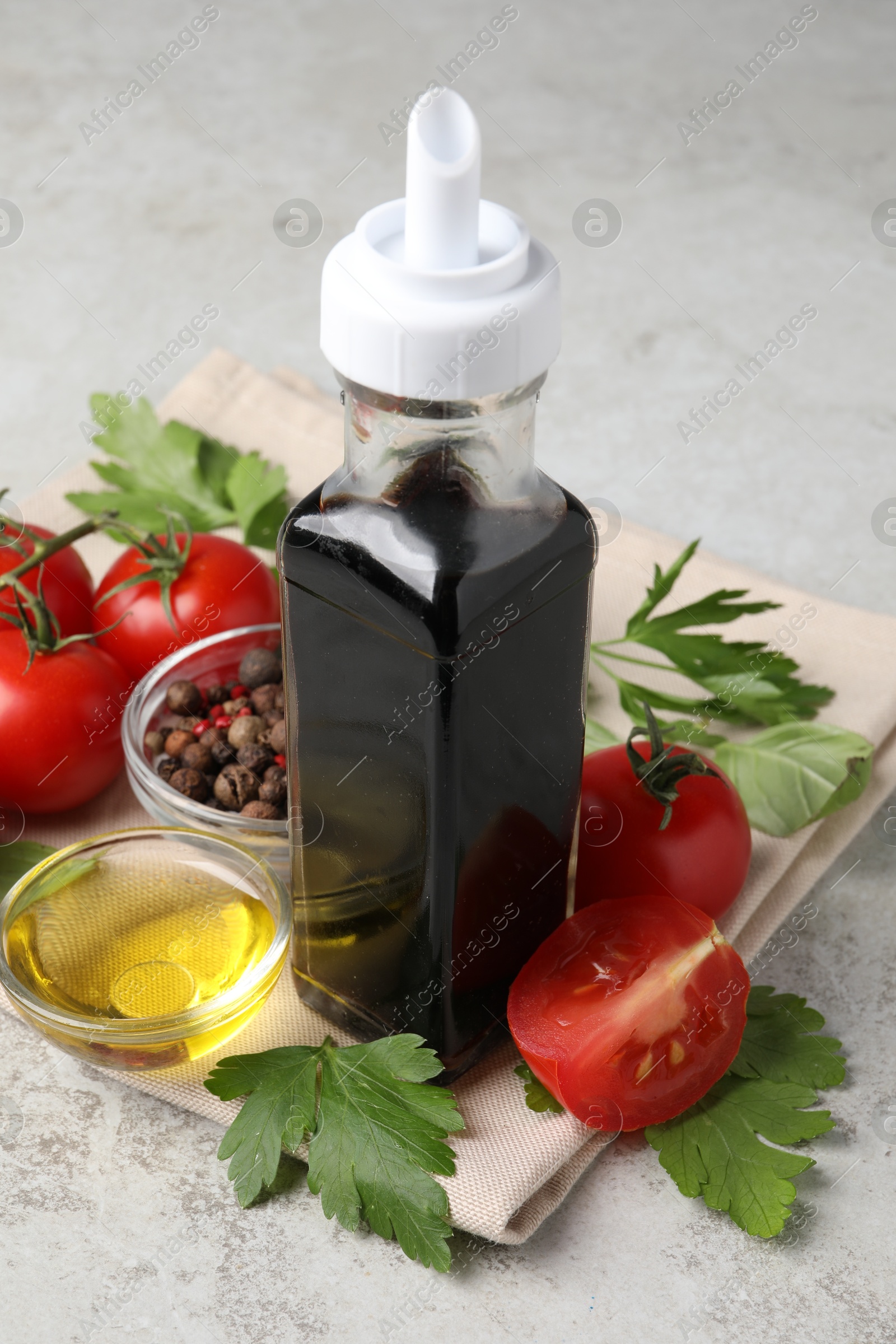 Photo of Bottle of balsamic vinegar, tomatoes, parsley and peppercorns on light grey table