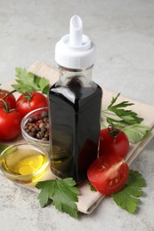 Bottle of balsamic vinegar, tomatoes, parsley and peppercorns on light grey table