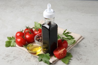 Photo of Bottle of balsamic vinegar, tomatoes, parsley and peppercorns on light grey table