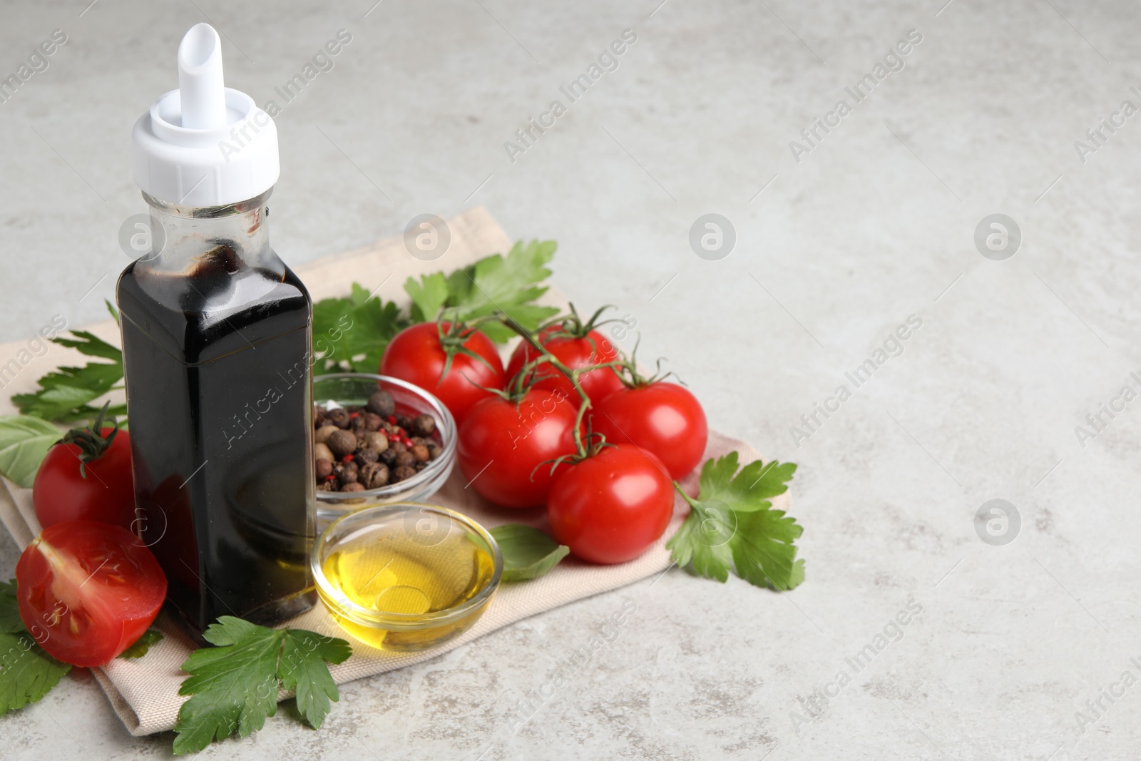 Photo of Bottle of balsamic vinegar, tomatoes, parsley and peppercorns on light grey table, space for text