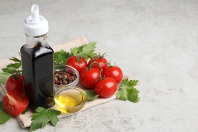 Bottle of balsamic vinegar, tomatoes, parsley and peppercorns on light grey table, space for text