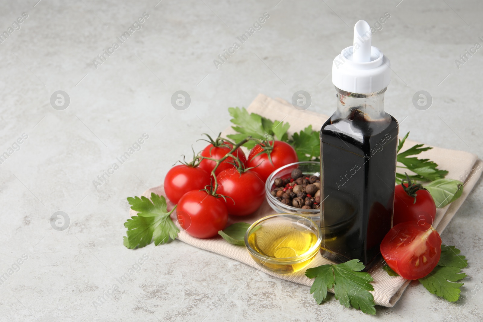 Photo of Bottle of balsamic vinegar, tomatoes, parsley and peppercorns on light grey table, space for text