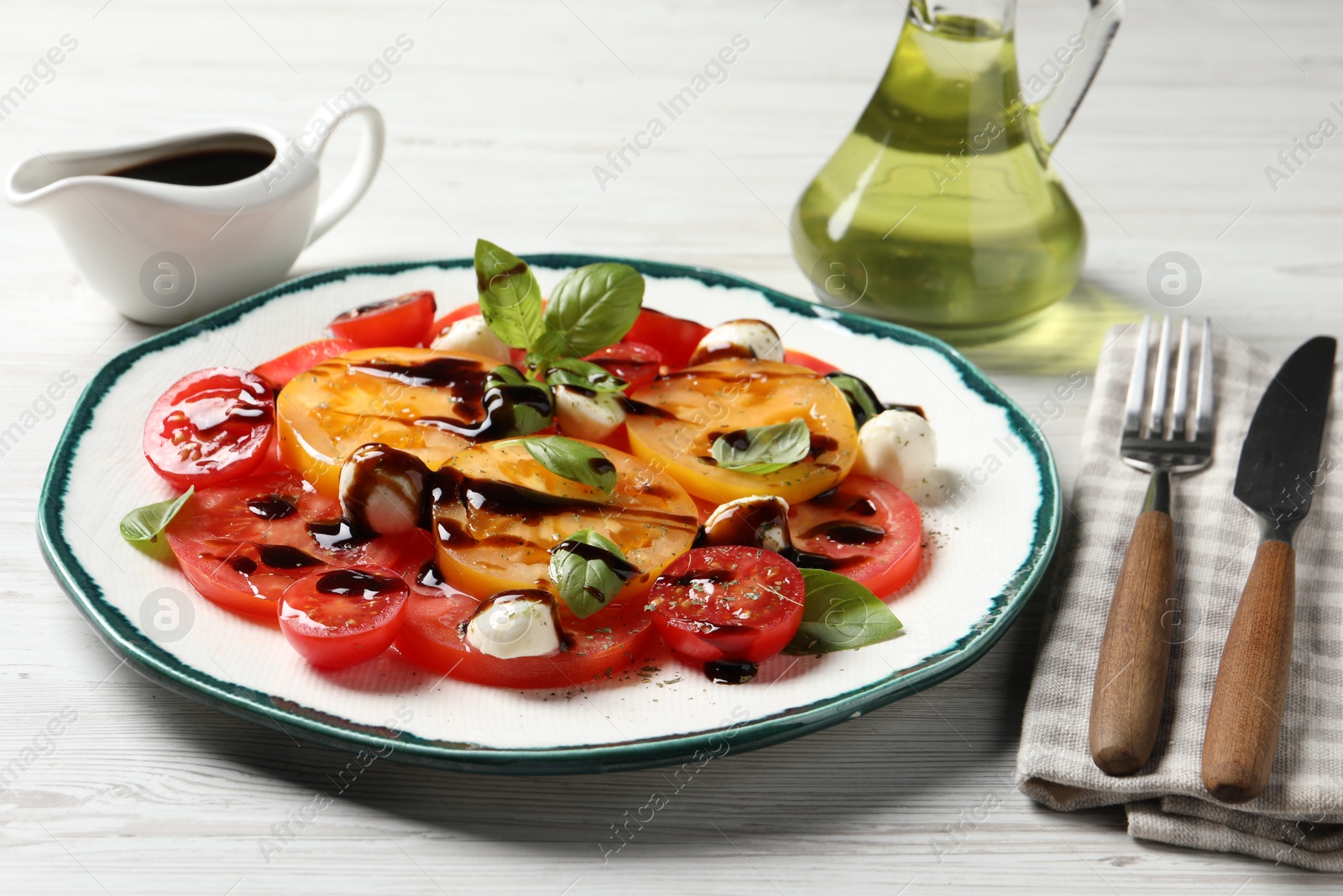 Photo of Tasty salad with balsamic vinegar, mozzarella and cutlery on white wooden table