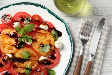 Tasty salad with balsamic vinegar, mozzarella and cutlery on white wooden table, flat lay