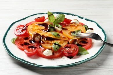 Photo of Tasty salad with balsamic vinegar, mozzarella and fork on white wooden table, closeup