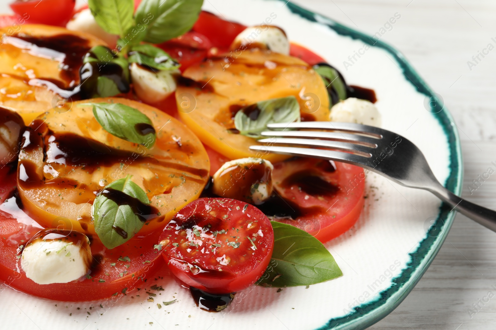 Photo of Tasty salad with balsamic vinegar, mozzarella and fork on white wooden table, closeup