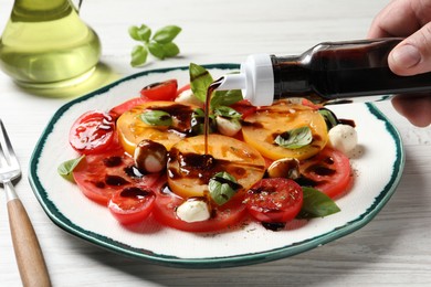 Woman pouring balsamic vinegar onto tasty salad at white wooden table, closeup