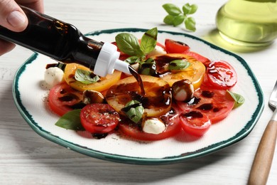 Photo of Woman pouring balsamic vinegar onto tasty salad at white wooden table, closeup