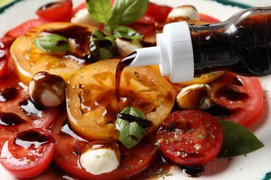 Pouring balsamic vinegar onto tasty salad on table, closeup