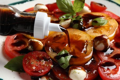 Photo of Pouring balsamic vinegar onto tasty salad on table, closeup