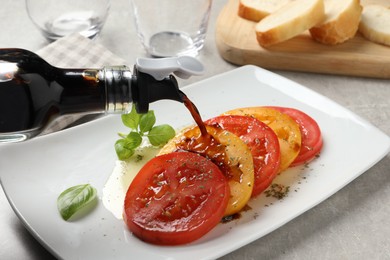 Pouring balsamic vinegar onto tasty salad on light grey table, closeup