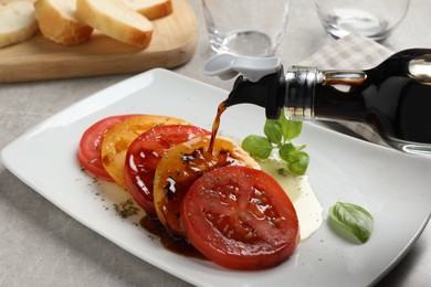 Pouring balsamic vinegar onto tasty salad on light grey table, closeup