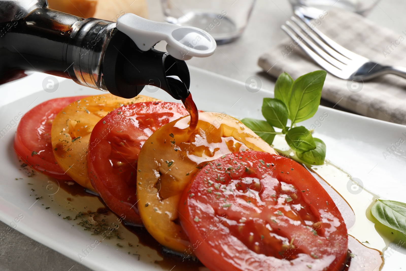 Photo of Pouring balsamic vinegar onto tasty salad on light grey table, closeup