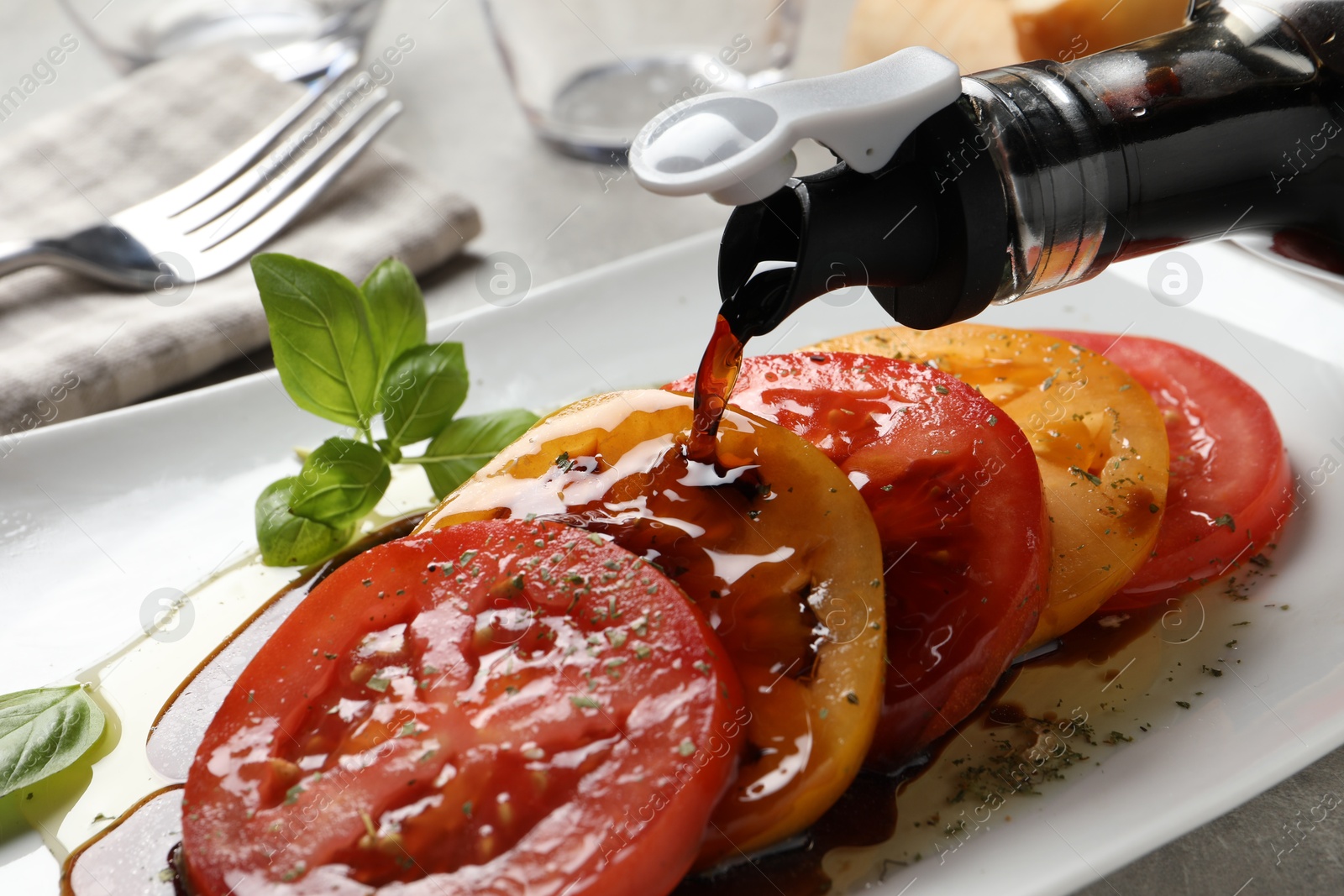 Photo of Pouring balsamic vinegar onto tasty salad on light grey table, closeup