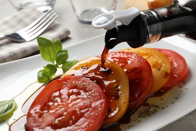 Pouring balsamic vinegar onto tasty salad on light grey table, closeup