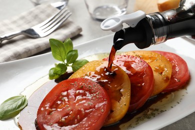 Pouring balsamic vinegar onto tasty salad on light grey table, closeup