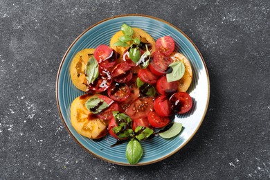 Photo of Tasty salad with balsamic vinegar and basil on black textured table, top view