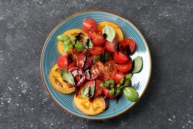 Tasty salad with balsamic vinegar and basil on black textured table, top view