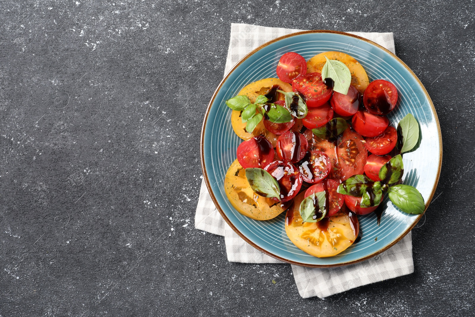 Photo of Tasty salad with balsamic vinegar and basil on black textured table, top view. Space for text