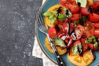 Photo of Tasty salad with balsamic vinegar, basil and fork on black textured table, top view. Space for text