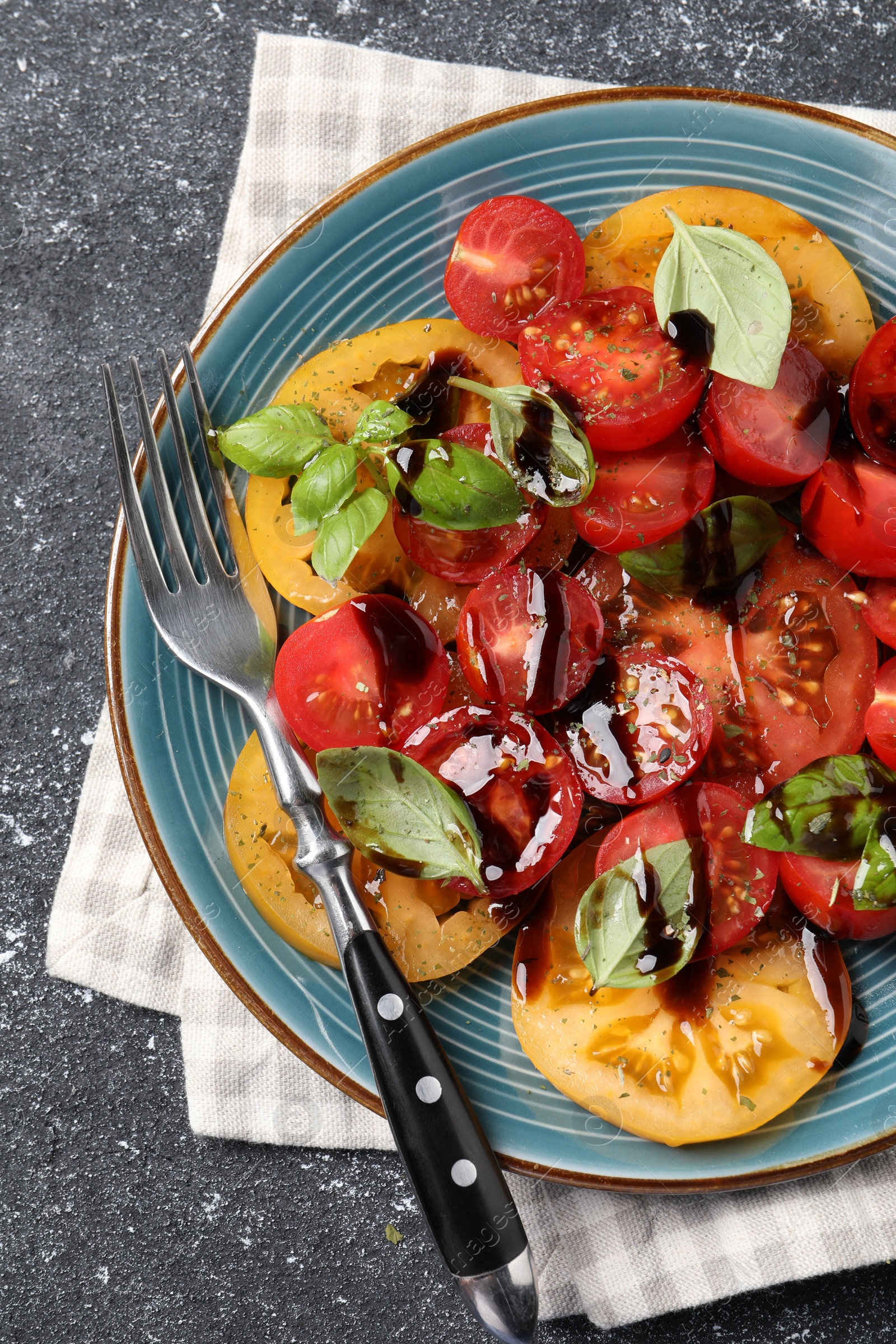 Photo of Tasty salad with balsamic vinegar, basil and fork on black textured table, top view