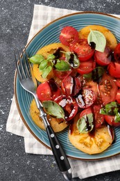 Tasty salad with balsamic vinegar, basil and fork on black textured table, top view