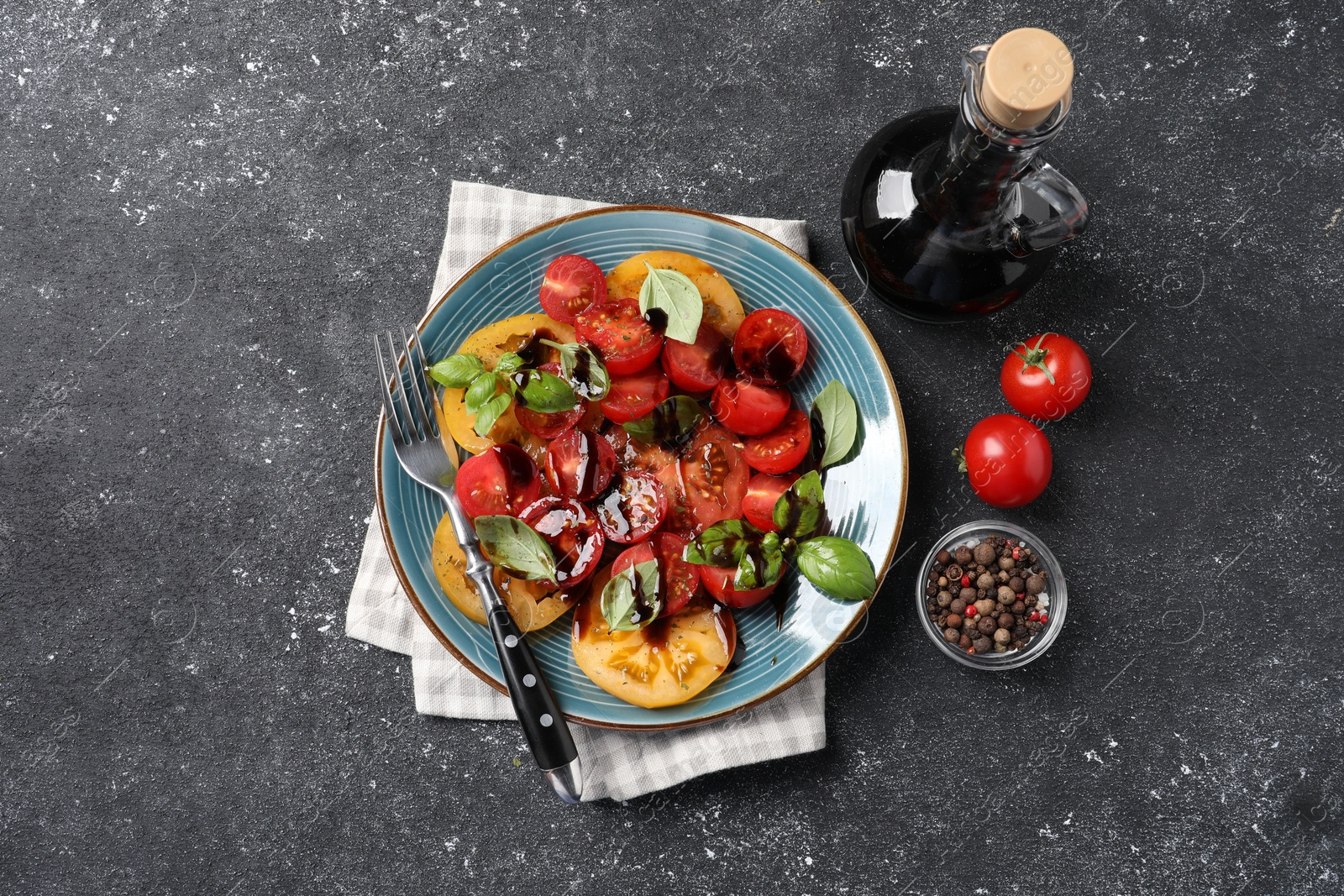 Photo of Tasty salad with balsamic vinegar, basil and fork on black textured table, flat lay