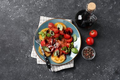 Tasty salad with balsamic vinegar, basil and fork on black textured table, flat lay