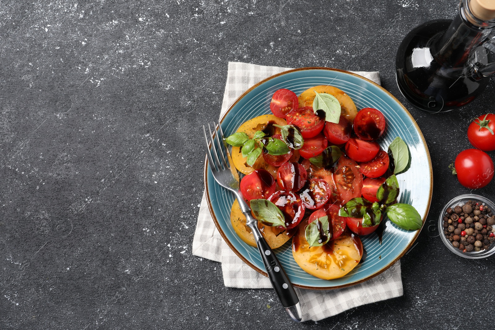 Photo of Tasty salad with balsamic vinegar, basil and fork on black textured table, flat lay. Space for text