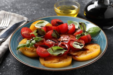 Photo of Tasty salad with balsamic vinegar, basil and fork on black textured table