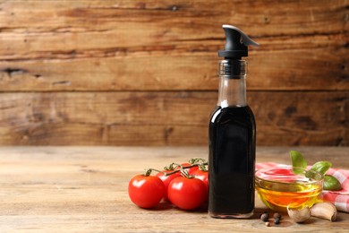 Bottle of balsamic vinegar, oil and other products on wooden table, space for text