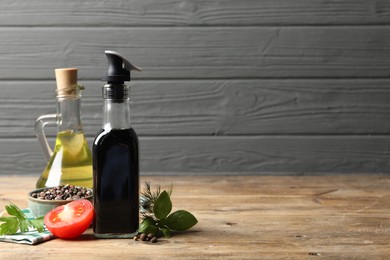 Photo of Bottle of balsamic vinegar, oil and other products on wooden table, space for text