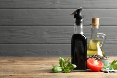 Bottle of balsamic vinegar, oil and other products on wooden table, space for text