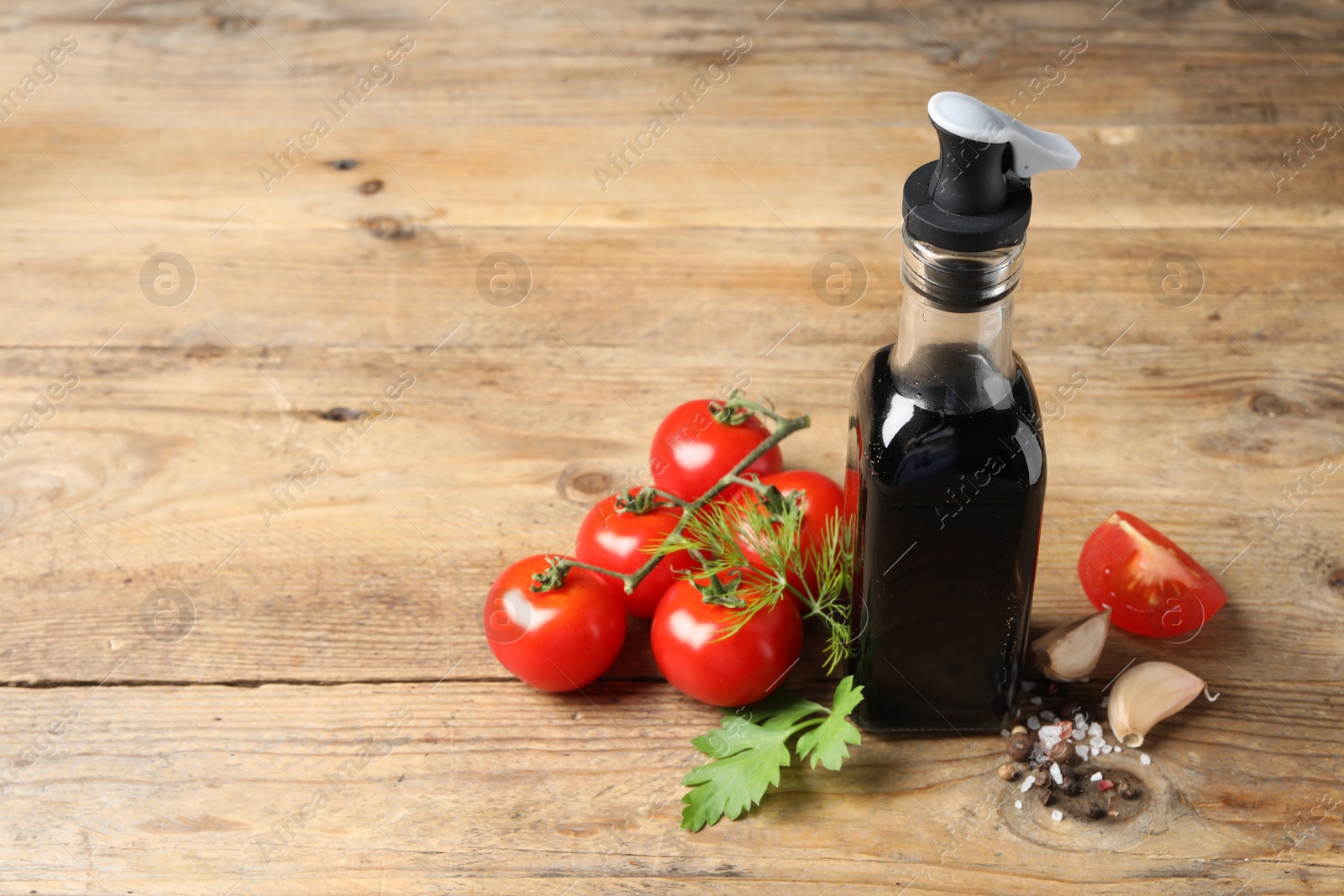 Photo of Bottle of balsamic vinegar, tomatoes and other products on wooden table, space for text