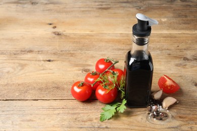 Bottle of balsamic vinegar, tomatoes and other products on wooden table, space for text