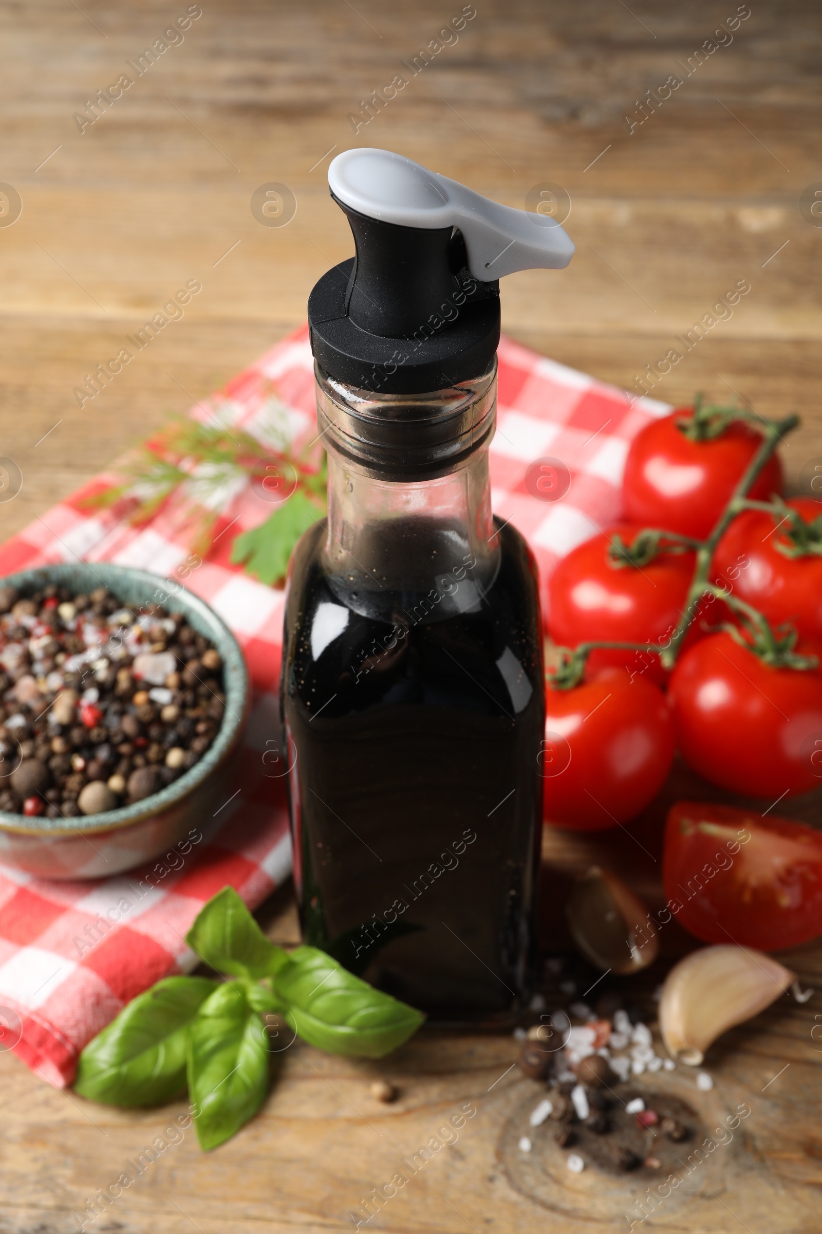 Photo of Bottle of balsamic vinegar, tomatoes and other products on wooden table