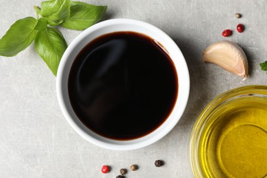 Photo of Balsamic vinegar, oil, garlic, peppercorns and basil on light grey table, flat lay