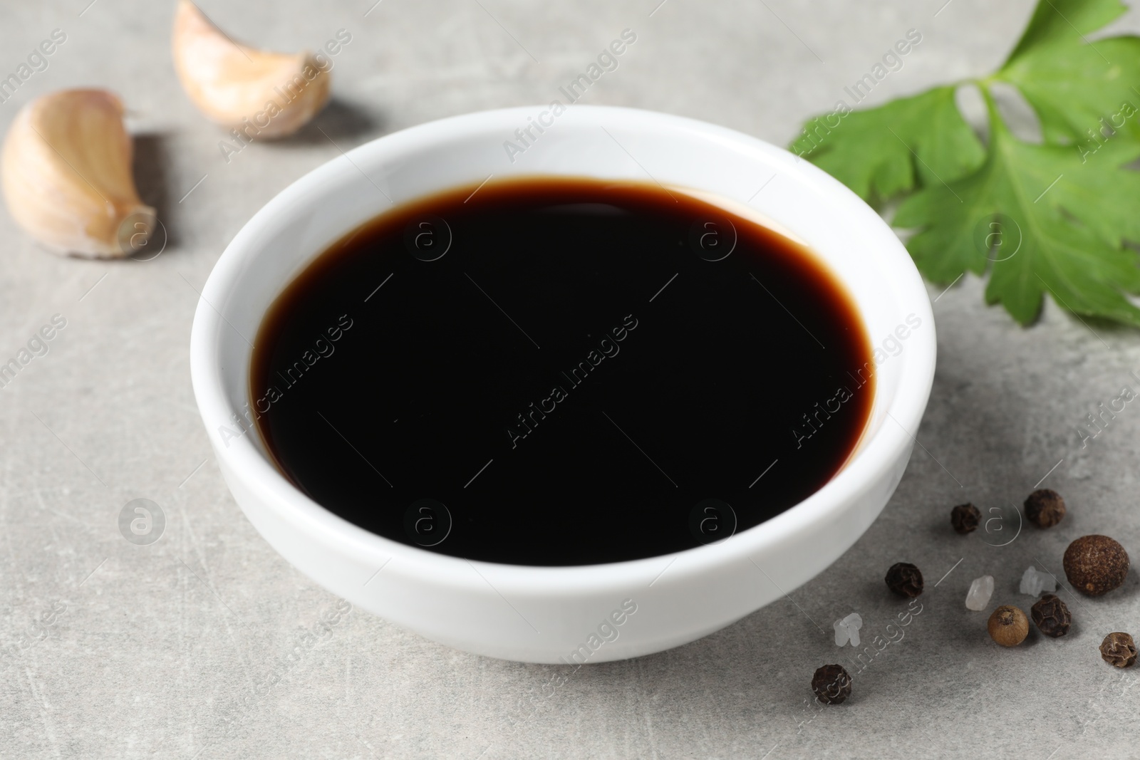 Photo of Balsamic vinegar, garlic, parsley and peppercorns on light grey table, closeup