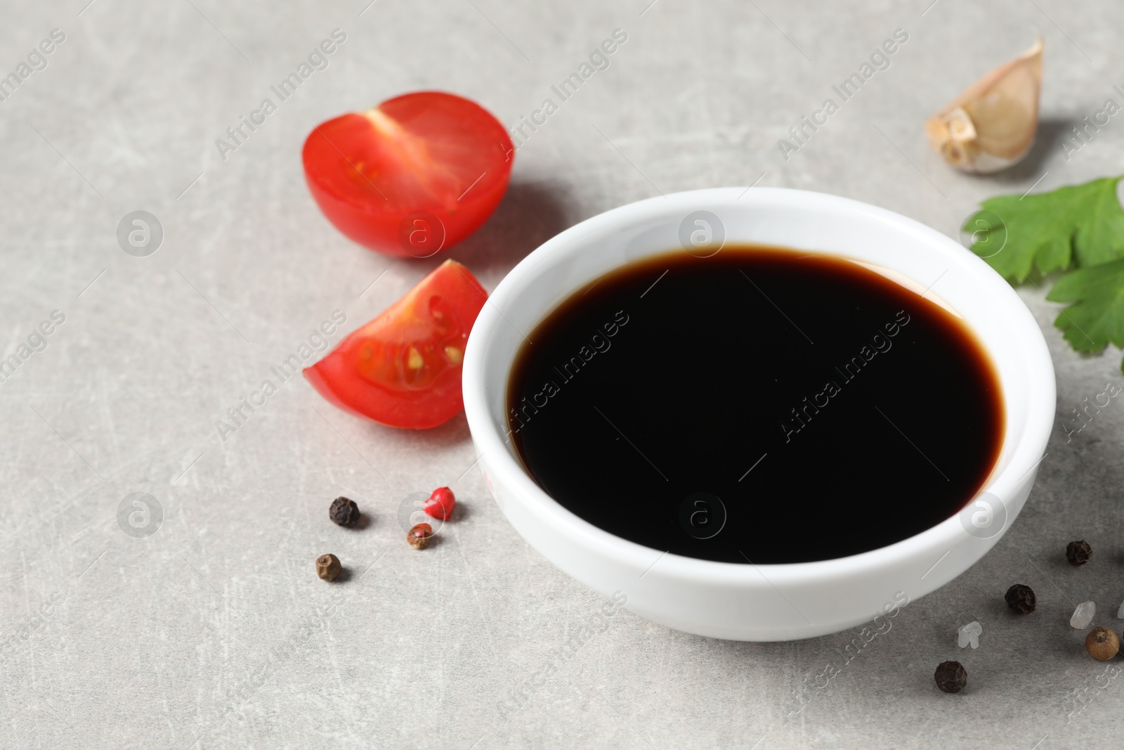 Photo of Balsamic vinegar, tomatoes, parsley and peppercorns on light grey table, closeup