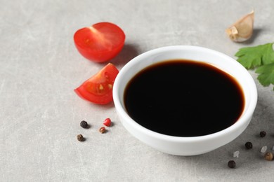 Balsamic vinegar, tomatoes, parsley and peppercorns on light grey table, closeup